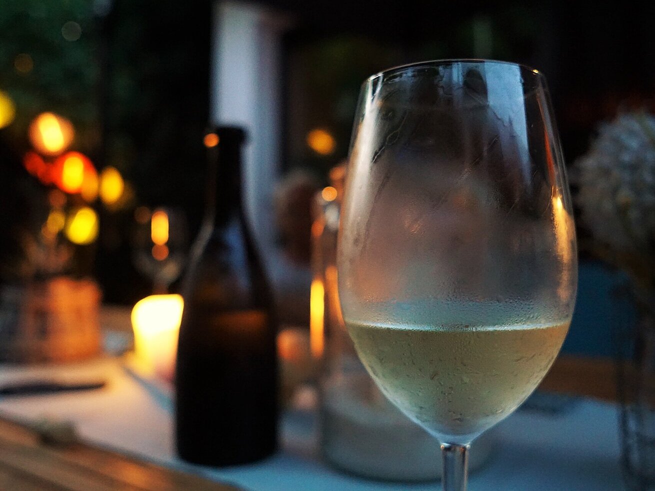Glas Weißwein Gekühltes Glas Weißwein auf einem Tisch bei stimmungsvoller Beleuchtung und Kerzenschein.