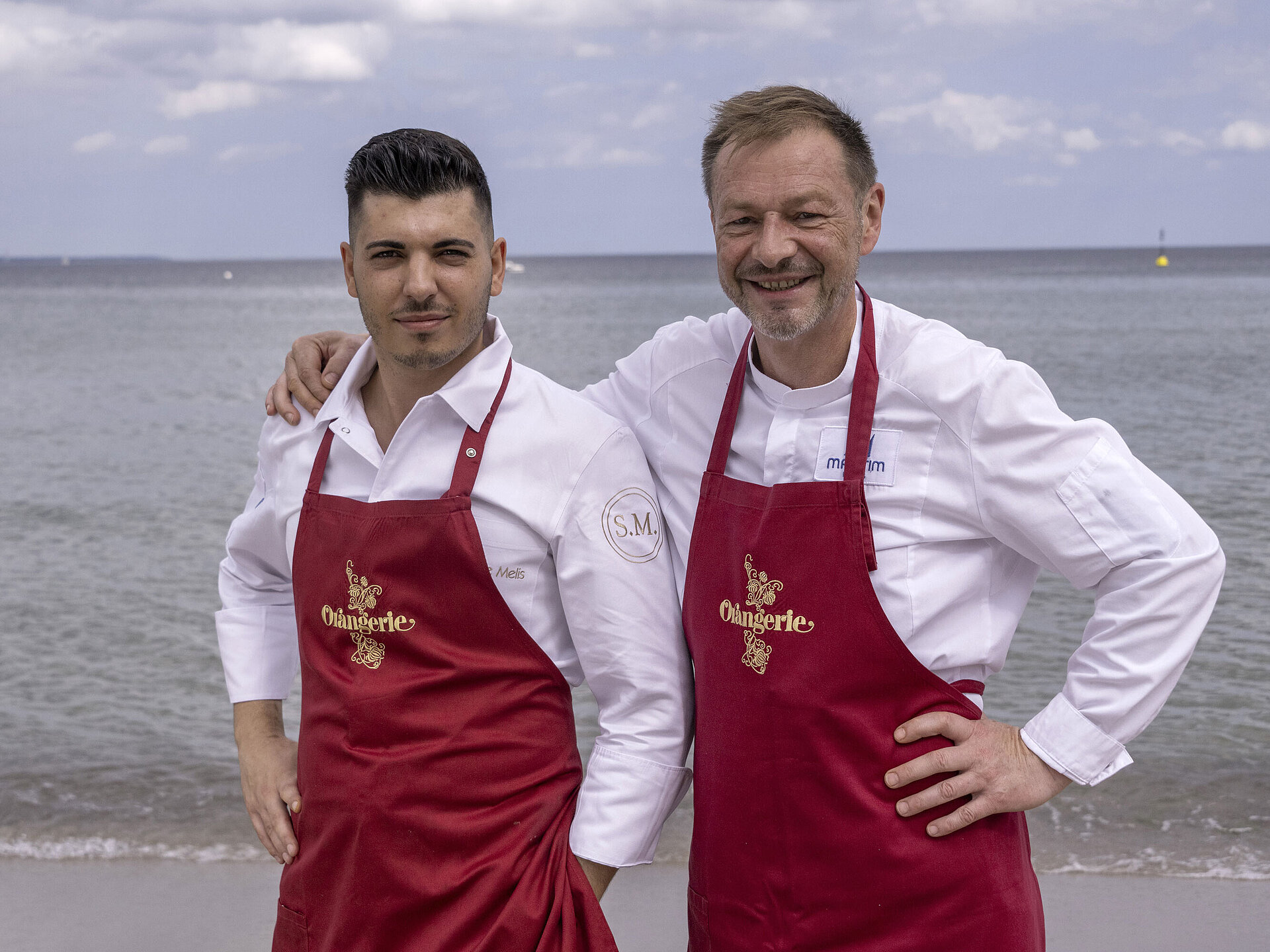 Küchenchefs Thomas Lemke und Simone Melis Küchenchefs Simone Melis und Thomas Lemke mit roten Schürzen am Meer vor dem Maritim Hotel Timmendorfer Strand.
