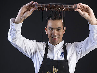 Chef Pâtissier Taro Bünemann Taro Bünemann, Chef Pâtissier der Orangerie im Maritim Timmendorfer Strand, hält ein Tablett, von dem Schokolade tropft.