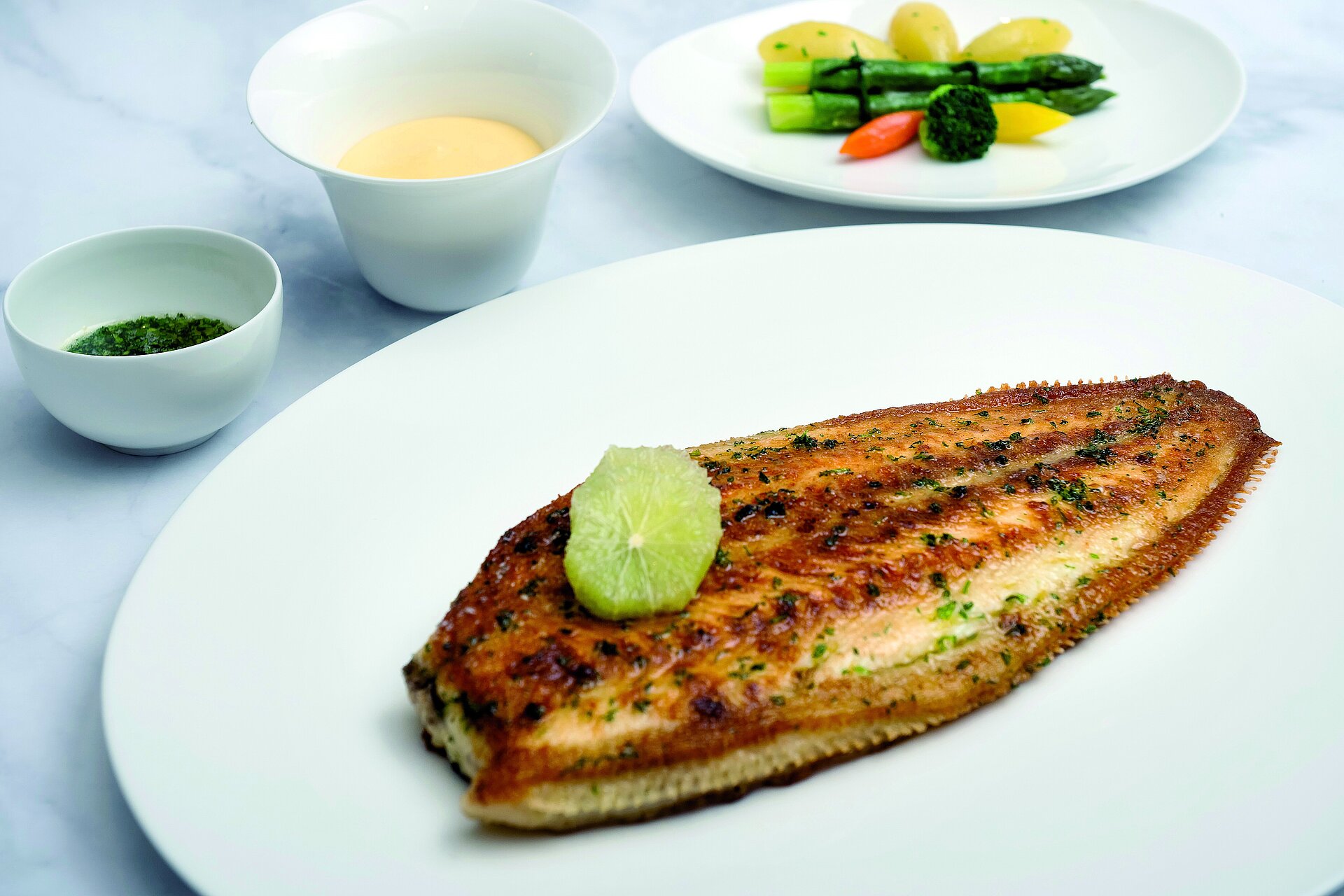 Gegrillte Seezunge mit Gemüse Gegrillte Seezunge mit Limette, Gemüsebeilage und Saucen auf weißem Teller angerichtet